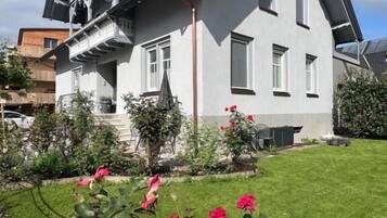 A two-story house with a balcony, a well-maintained lawn, and flowering plants.