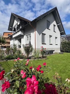 A two-story house with a balcony, a well-maintained lawn, and flowering plants. - Villa Rebgarten (Höchst)