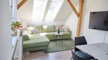 A cozy loft bedroom with a green sofa, a small round table, and a TV mounted on the wall.