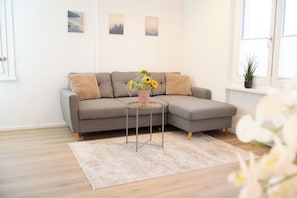 A modern living room with a grey sectional sofa, a small round table with a vase of flowers, and a white rug. - Villa Rebgarten (Höchst)