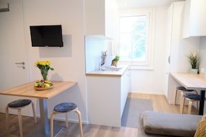 A compact kitchen with a dining area, a flat-screen TV mounted on the wall, and a window providing natural light. - Villa Rebgarten (Höchst)