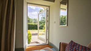 Une pièce dotée d’une porte-fenêtre coulissante donnant sur un jardin, d’un canapé agrémenté d’un coussin à motifs et d’une petite table sur laquelle repose un livre.