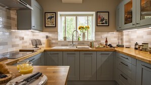 Une cuisine avec des meubles de couleur grise, un plan de travail en bois, une fenêtre avec des stores et un vase rempli de fleurs.