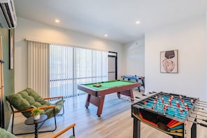 Ein Zimmer mit Poolbillardtisch, Kicker und einer Couch.