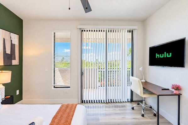 Ein Hotelzimmer mit Bett, Schreibtisch, an der Wand montiertem Fernseher und einer Schiebetür zum Balkon.