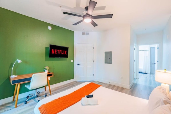 Ett hotellrum med en säng, ett skrivbord, en stol, en takfläkt och en väggmonterad TV som visar Netflix-logotypen.