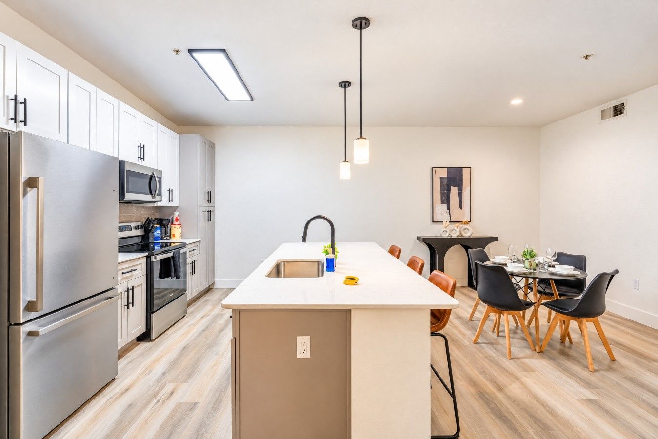 A modern kitchen with stainless steel appliances, a central island, and a dining area with chairs and a table.