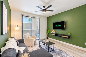 A living room with a sofa, a chair, a coffee table, a TV mounted on the wall, and a ceiling fan. - Westgate Escape  Pool, Gym & Walk to Stadium (Glendale)