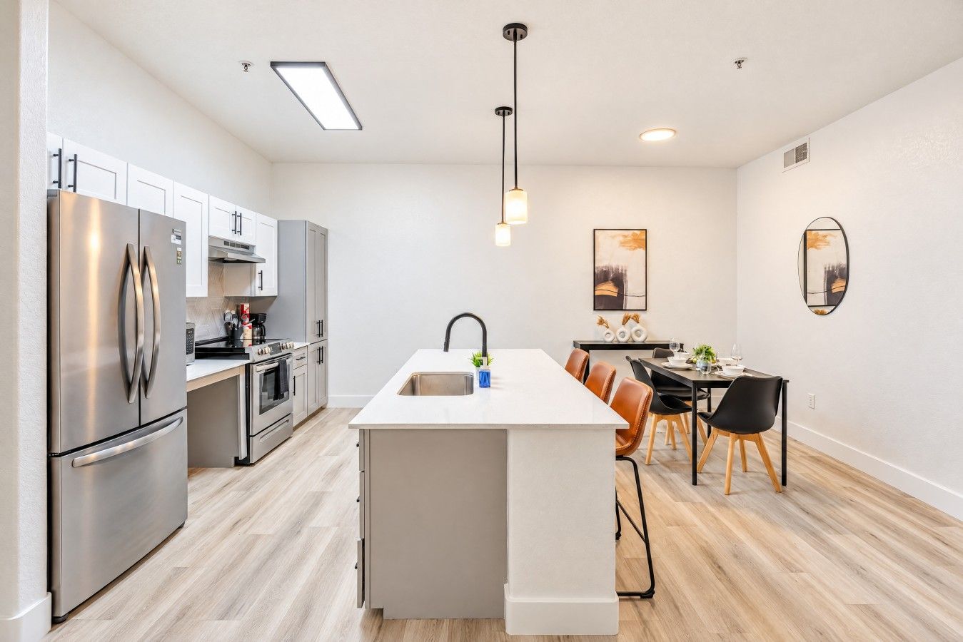 A modern kitchen with stainless steel appliances, a central island with a sink, and a dining area with a table and chairs.