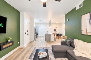Un salon moderne avec un canapé gris, une table basse sur laquelle sont posés des livres et un téléviseur fixé au mur.