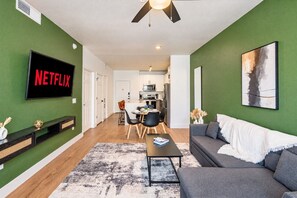 Ein modernes Wohnzimmer mit einem grauen Sofa, einem Couchtisch und einem Fernseher, der 'NETFLIX' zeigt.