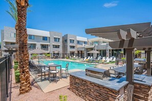 A pool area with lounge chairs, a barbecue, and a stone wall. - State Farm Stadium Condo Westgate Pool Parking WD (Glendale)