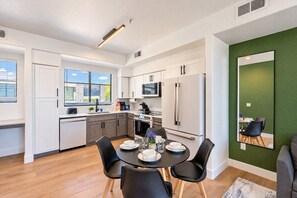 A modern kitchen with white cabinets, a dining table with black chairs, and a green accent wall. - Modern Westgate Condo  Pool Gym Parking WD (Glendale)
