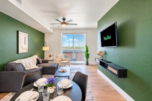 Een moderne woonkamer met een groene wand, een flatscreen televisie, een plafondventilator en een eethoek klaar voor een maaltijd.