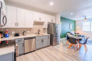 A modern kitchen with stainless steel appliances, a dishwasher, and a dining area with a table and chairs. - Westgate Stadium Stay  Pool Gym WD Parking (Glendale)