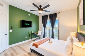 Ein Hotelzimmer mit Bett, Schreibtisch, Wandfernseher und Deckenventilator.