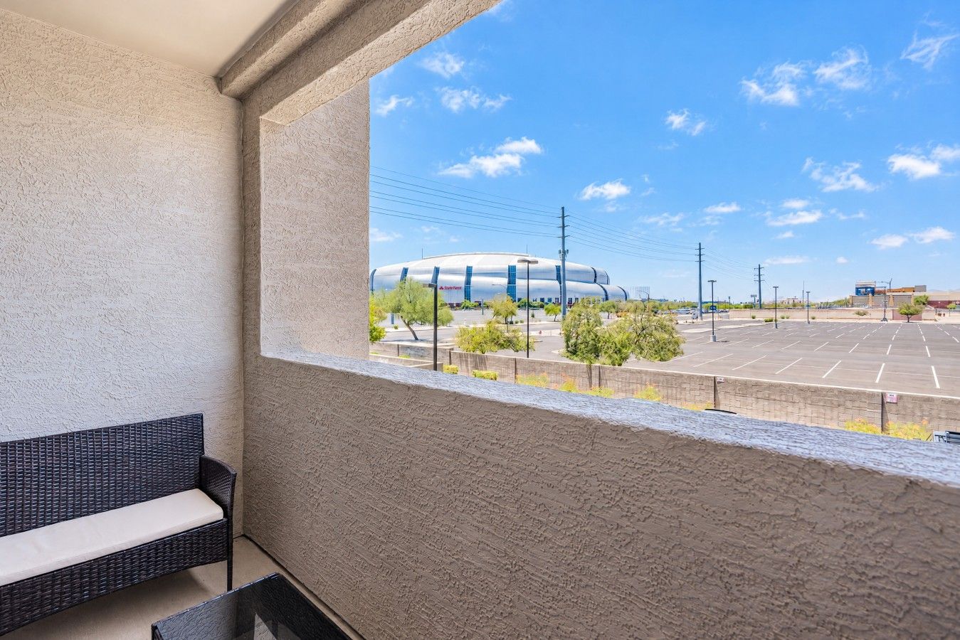 Un balcone con una sedia in vimini, vista su un parcheggio e un edificio con tetto curvo.