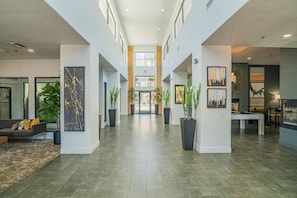 Eine großzügige Lobby mit hoher Decke, einer zentralen Treppe und einem Poolbereich, der durch Glastüren sichtbar ist.