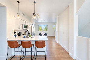 A modern kitchen with a central island, bar stools, pendant lighting, and a view to a dining area. - Stadium District Retreat Pool, Gym & Westgate (Glendale)