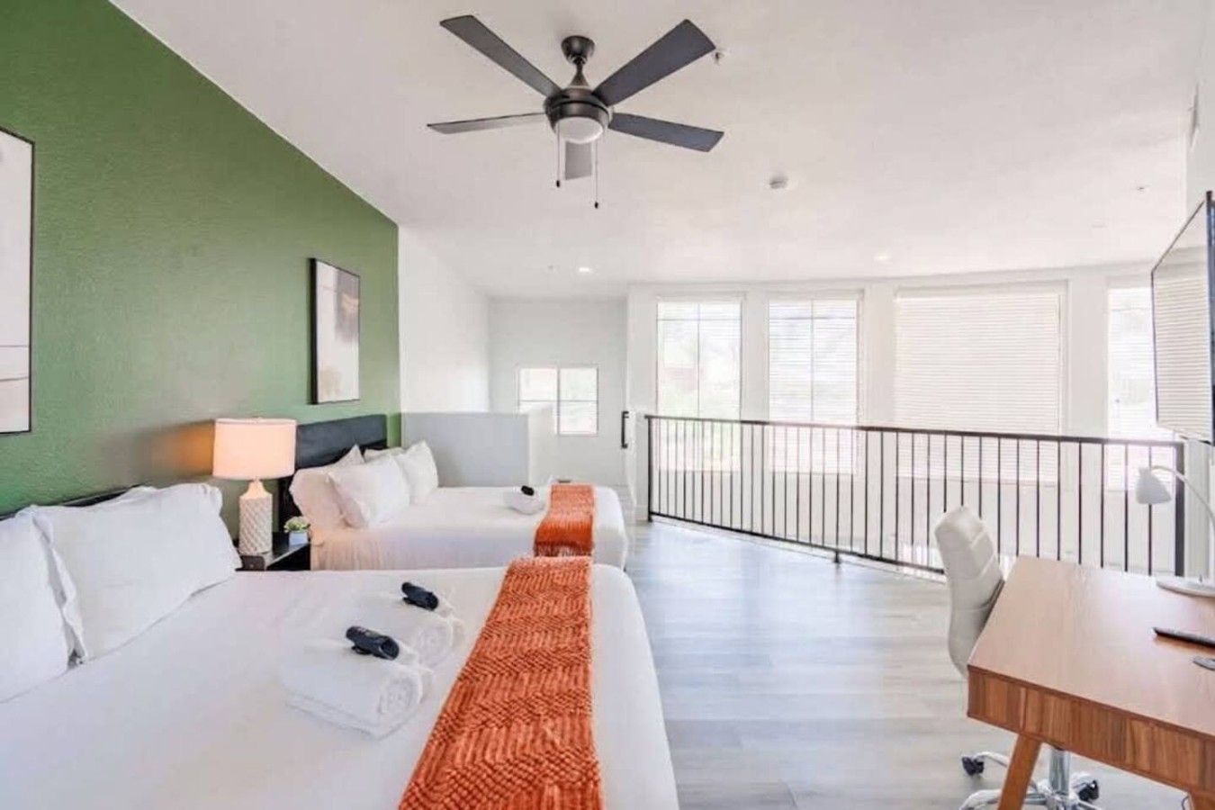 A hotel room with two beds, a desk, a balcony, and a ceiling fan.