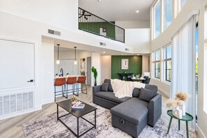 A spacious living area with a high ceiling, a dining area with a green accent wall, and a balcony with a railing. - Glendale Westgate Stay  Pool Gym WD Near Stadium (Glendale)