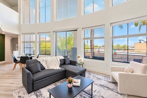 Ein geräumiges Wohnzimmer mit einer Eckcouch, einem Couchtisch und Blick ins Freie durch große Fenster.