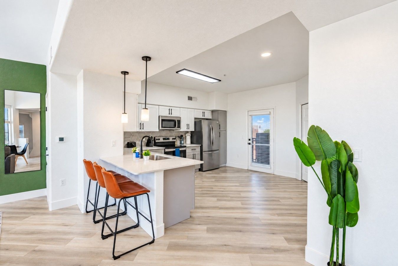 A modern kitchen with a central island, stainless steel appliances, and a green accent wall.