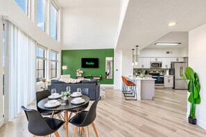 A modern apartment with a dining area, a living room with a green accent wall, a kitchen, and a large window. - Glendale Westgate Stay  Pool Gym WD Near Stadium (Glendale)