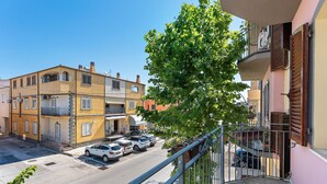 Eine Wohnstraße mit mehrstöckigen Gebäuden, parkenden Autos und einem Balkon mit Metallgeländer.
