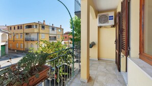 Ein Balkon mit einem Blumentopf, ein geparktes Auto davor und ein Gebäude mit einer gelben Fassade im Hintergrund.