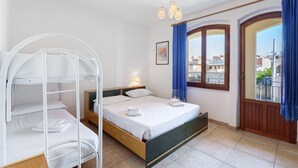 Ein Zimmer mit Etagenbett, einem Einzelbett, einem Fenster mit Vorhängen, einer Nachttischlampe und Blick auf Gebäude.