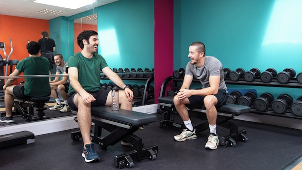 Uma academia com equipamentos de musculação, bancos e espelhos.