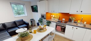 A modern kitchen with white cabinets, a dining table with a white tablecloth, and a black leather sofa. - Student Only Adam Street Gardens (Cardiff)