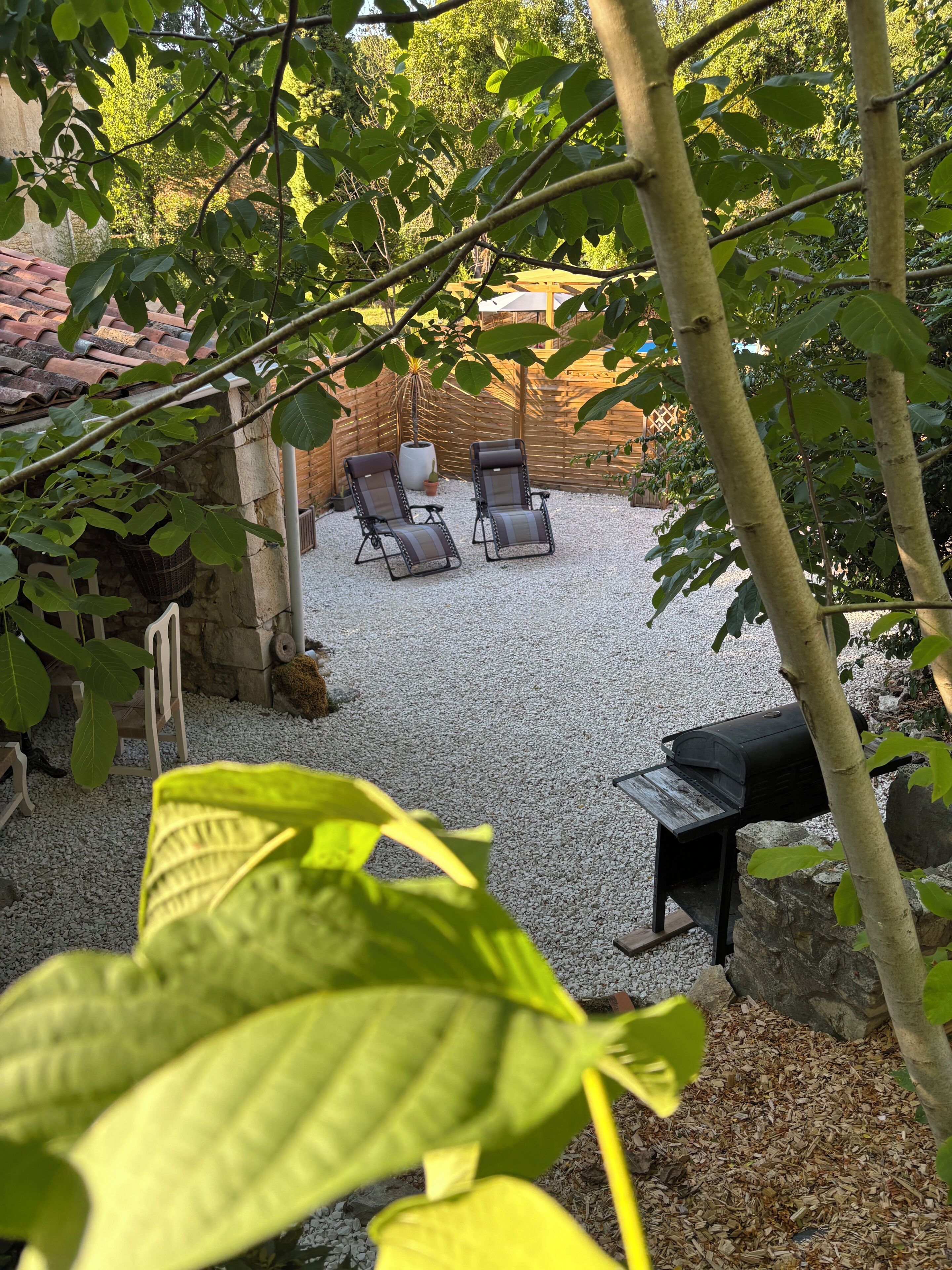 Un espace patio comprenant deux chaises longues, un barbecue et un mur en pierre.