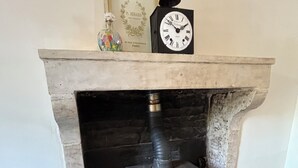 Ein Kamin mit einer darüber hängenden Uhr, ein gerahmtes Schild darüber und ein Korbwägelchen zur Rechten.