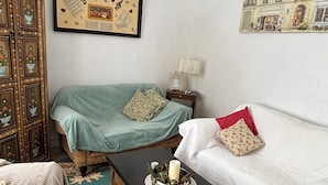 Ein Zimmer mit einem Bett, einem Sessel, einem Tisch mit Kerzen, einer Lampe und einem gerahmten Bild an der Wand.