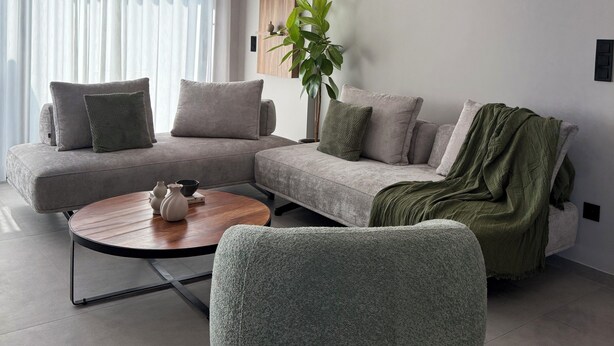 Una sala de estar moderna con un sofá modular, una mesa de centro redonda, un sillón verde y una planta en maceta.