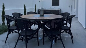 Una mesa redonda al aire libre con seis sillas negras, un farol de metal y una parrilla integrada.