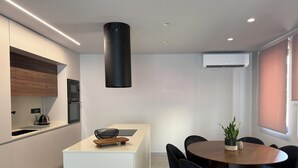 Una cocina moderna con una isla central, un comedor con mesa y sillas redondas, y un equipo de aire acondicionado en la pared.