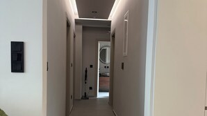 Un pasillo estrecho y bien iluminado, de diseño moderno, que conduce a una habitación con un espejo grande y una puerta.