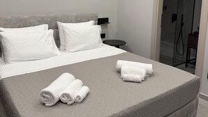 Habitación de hotel moderna con una cama grande, una mesita de noche, aire acondicionado montado en la pared y cabina de ducha de vidrio.