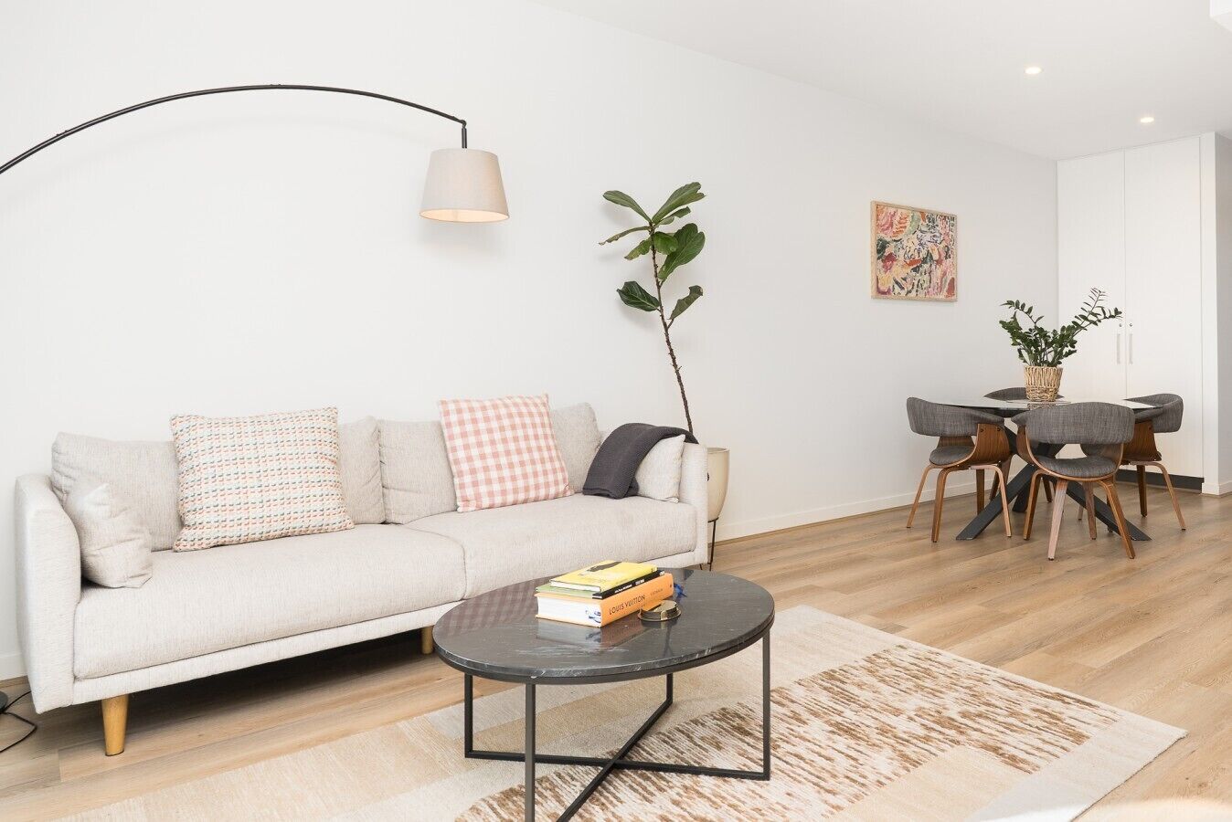 A modern living room with a sofa, a coffee table, a dining area with chairs, and a lamp.