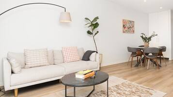 A modern living room with a sofa, a coffee table, a dining area with chairs, and a lamp.