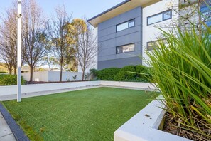A modern building with a flat roof, a well-maintained lawn, and a white wall with a security camera.