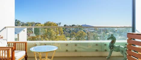 Un balcon doté d’une balustrade en verre, d’une table, de chaises et d’une statue équestre décorative.