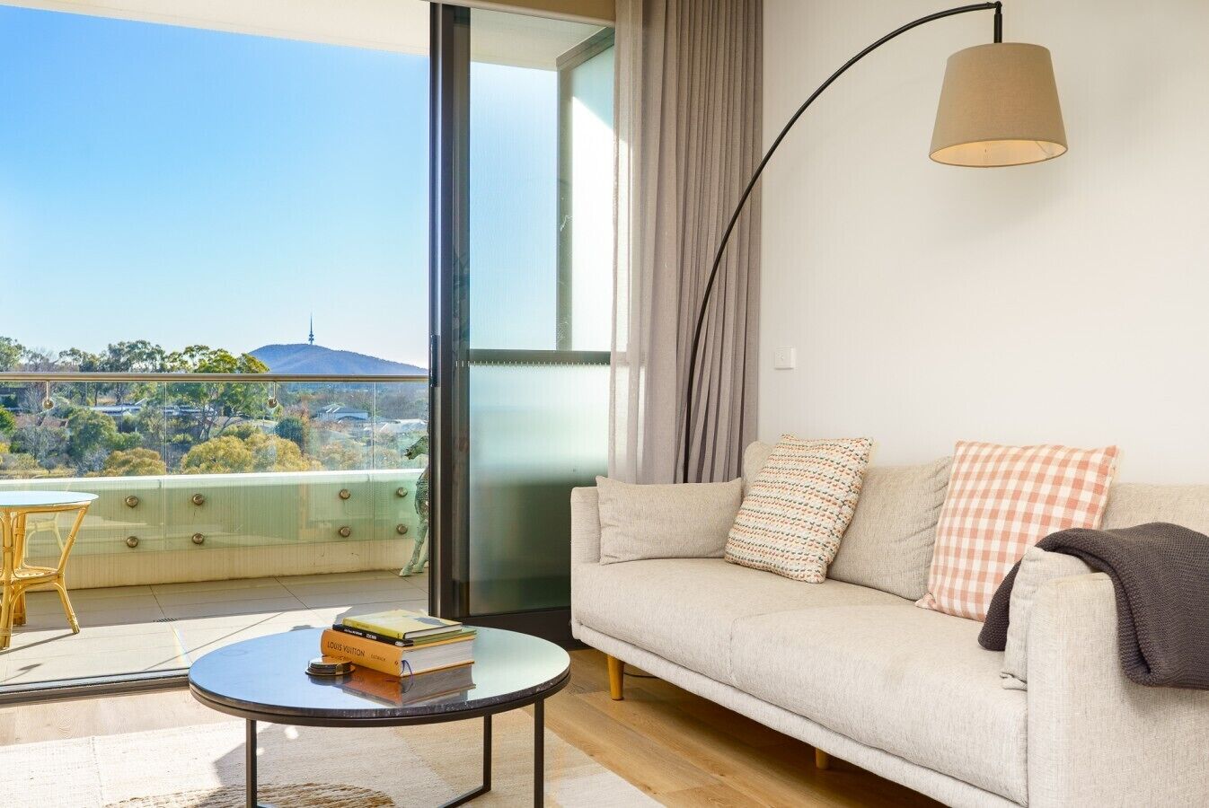 A modern living room with a sofa, a round coffee table, and a balcony with a view.