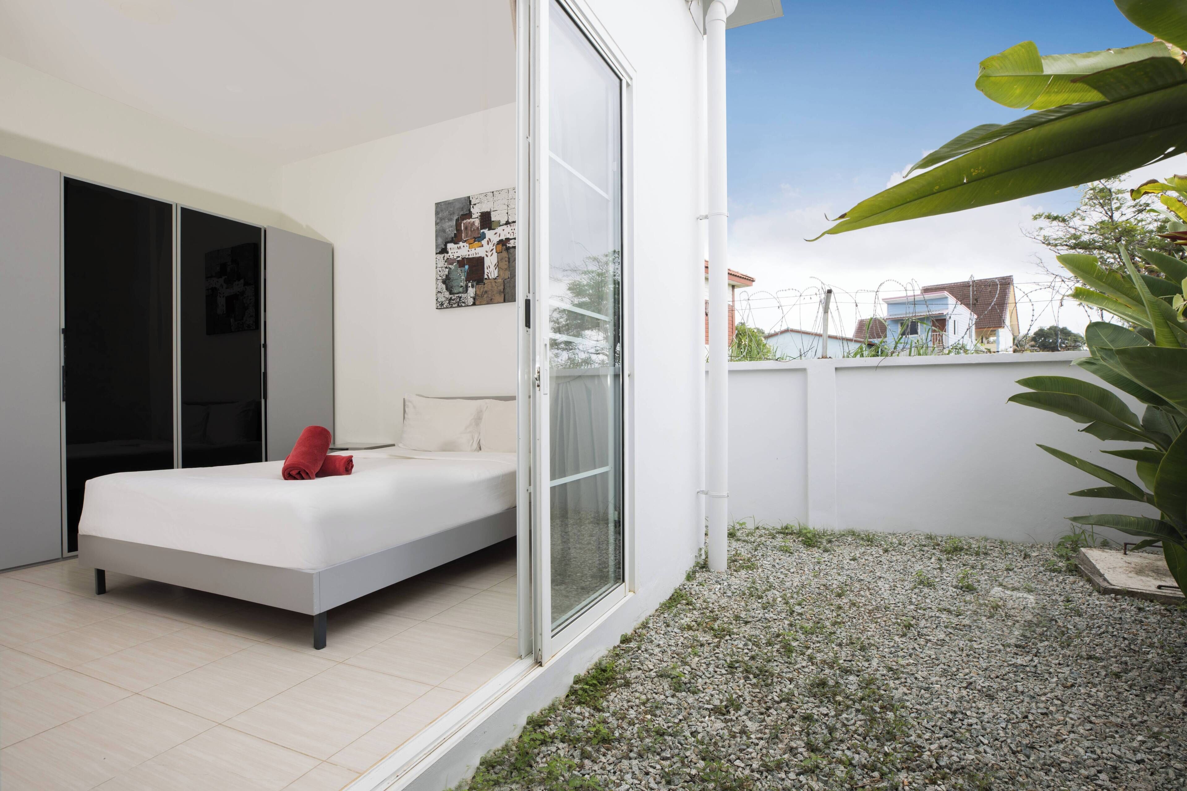 A modern bedroom with a bed, a sliding glass door to a balcony, and a small garden area.
