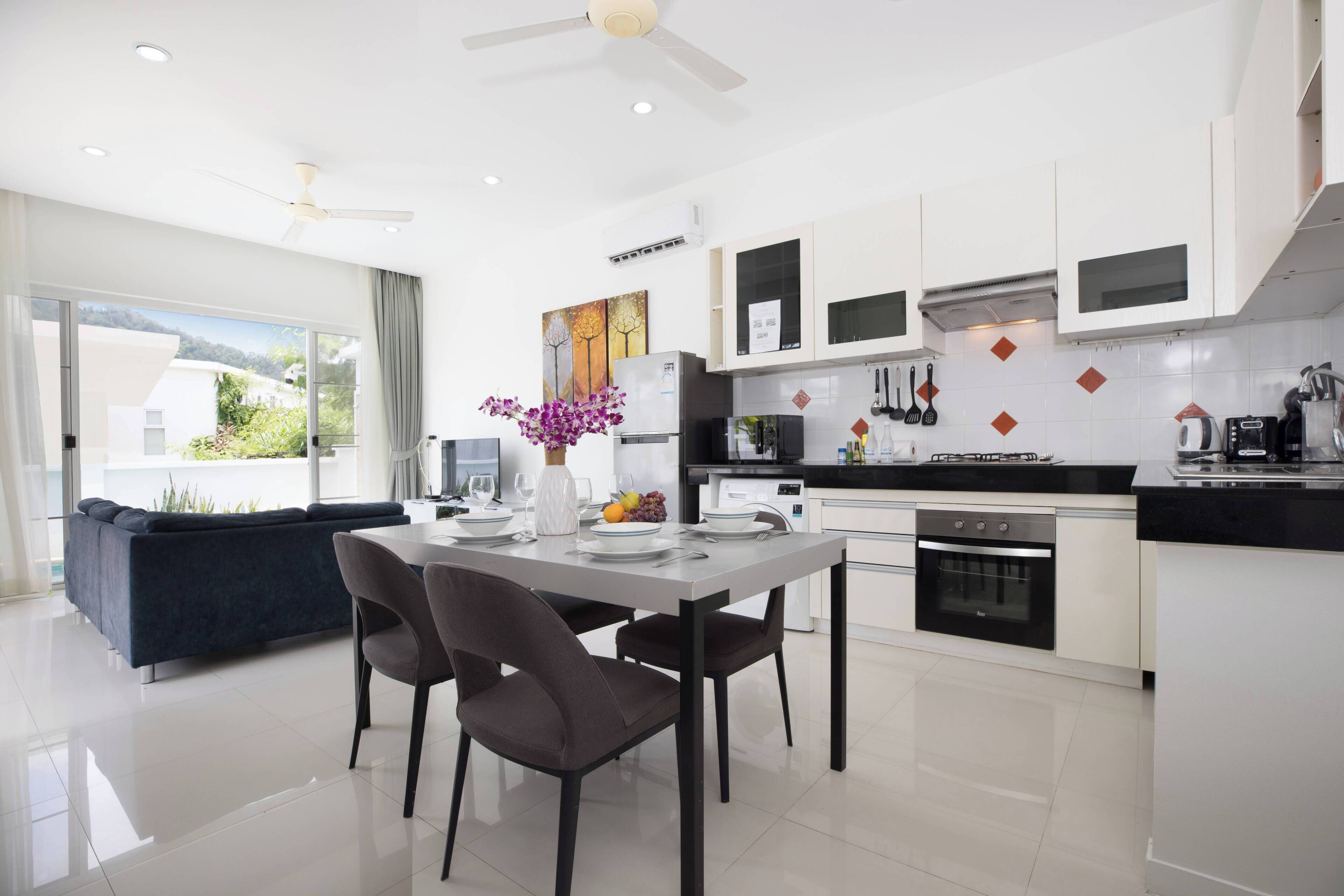 A modern kitchen with white cabinets, a dining table with chairs, and a large window with a view of greenery.