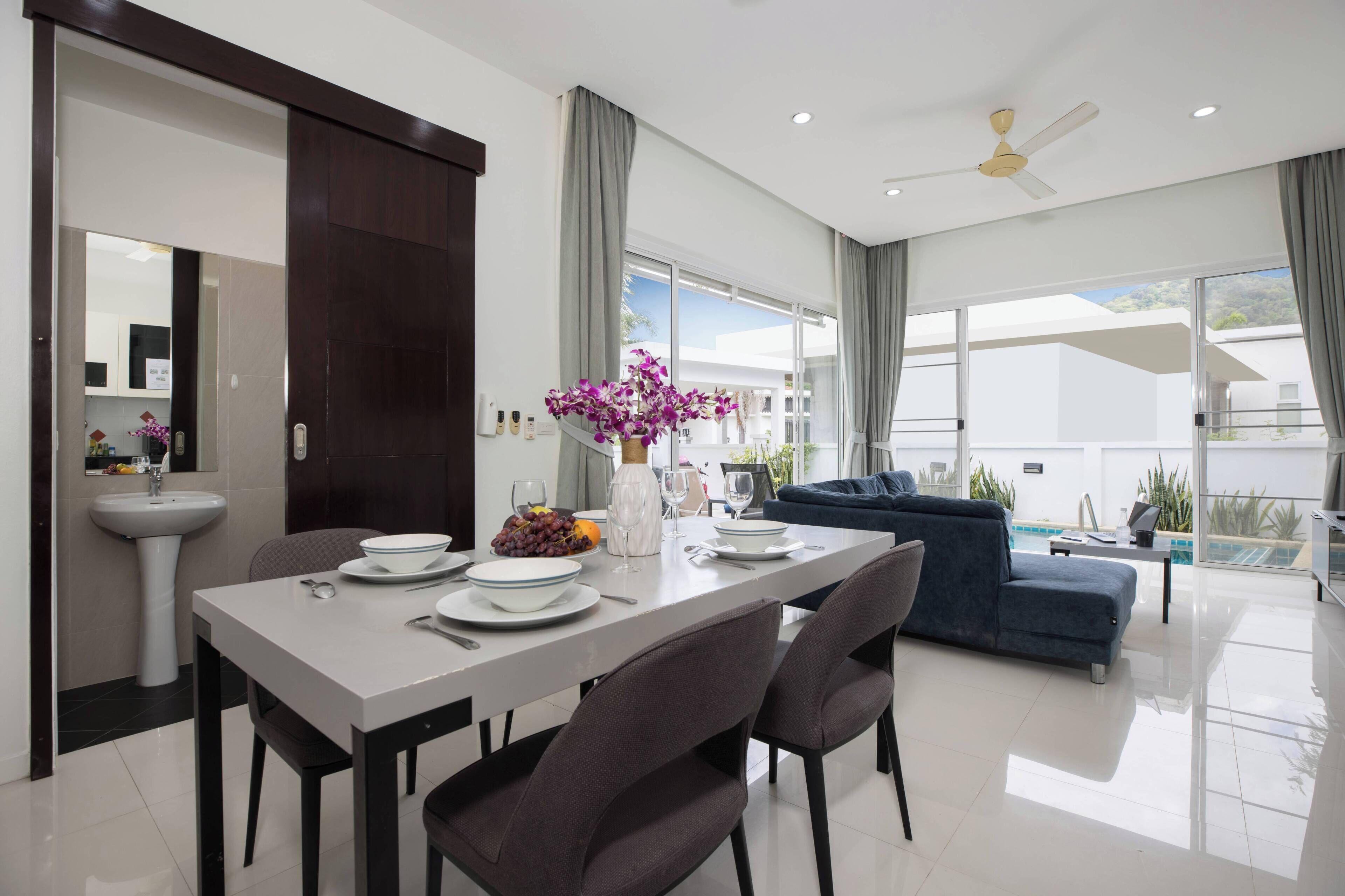A modern living room with a dining area, a sofa, a pool view, and a ceiling fan.