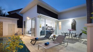 Et moderne hus med swimmingpool, liggestole, et spiseområde og et køkken, der kan ses gennem glasdøre.